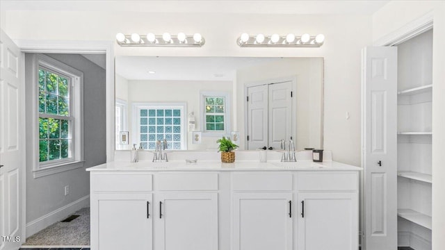 bathroom with double vanity, a closet, a sink, and baseboards