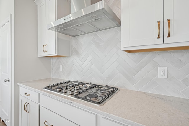 kitchen with stainless steel gas cooktop, white cabinets, ventilation hood, backsplash, and light stone countertops