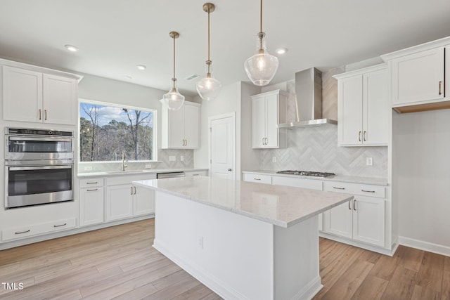 kitchen featuring light wood-style floors, wall chimney exhaust hood, stainless steel appliances, and a sink