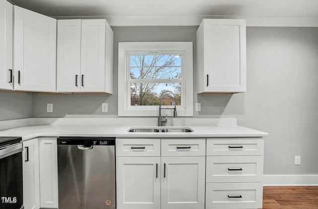 kitchen with light countertops, appliances with stainless steel finishes, white cabinetry, a sink, and wood finished floors