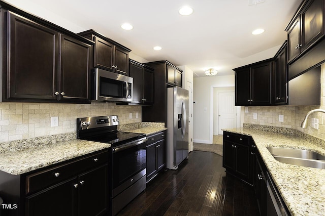 kitchen featuring baseboards, decorative backsplash, dark wood-style flooring, stainless steel appliances, and a sink