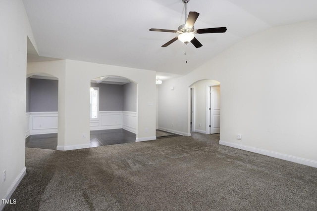 empty room with a wainscoted wall, vaulted ceiling, arched walkways, and dark colored carpet