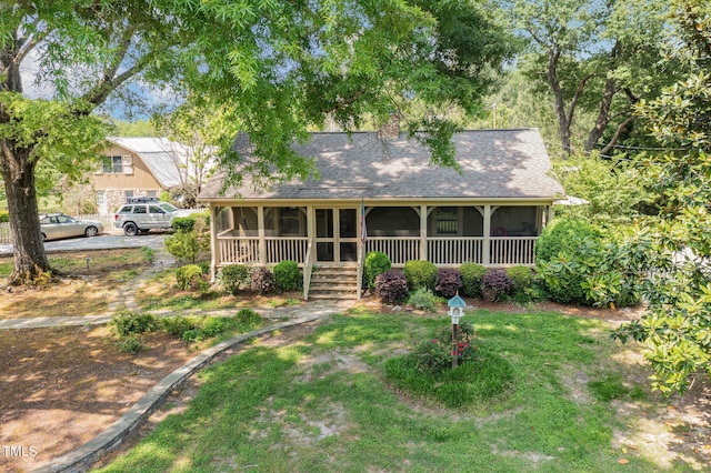 view of front of house featuring a shingled roof, a chimney, a front yard, and a sunroom