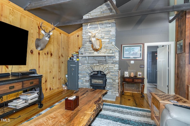 living area featuring lofted ceiling with beams, wood walls, wood finished floors, and a wood stove