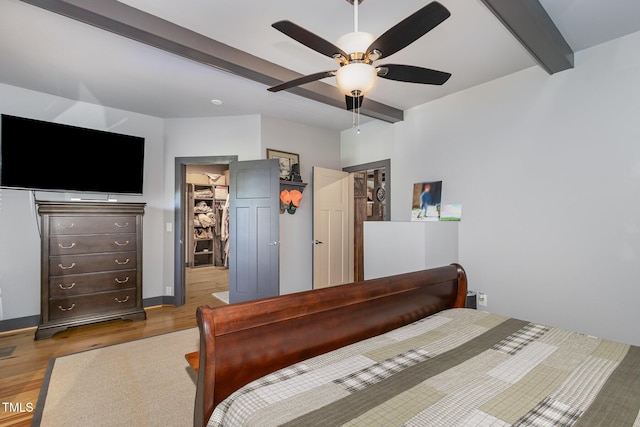 bedroom featuring a ceiling fan, beamed ceiling, wood finished floors, a walk in closet, and a closet