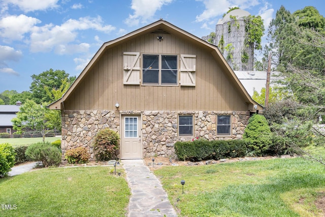 view of front of house featuring stone siding, a front lawn, and a gambrel roof