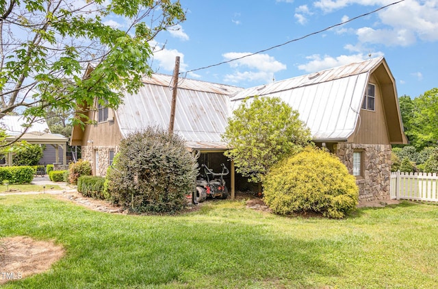 view of property exterior featuring a barn, fence, a gambrel roof, stone siding, and a lawn