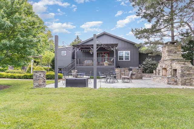 rear view of house featuring board and batten siding, an outdoor stone fireplace, a patio, and a lawn