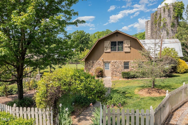 view of side of home featuring stone siding, fence, a gambrel roof, and a lawn