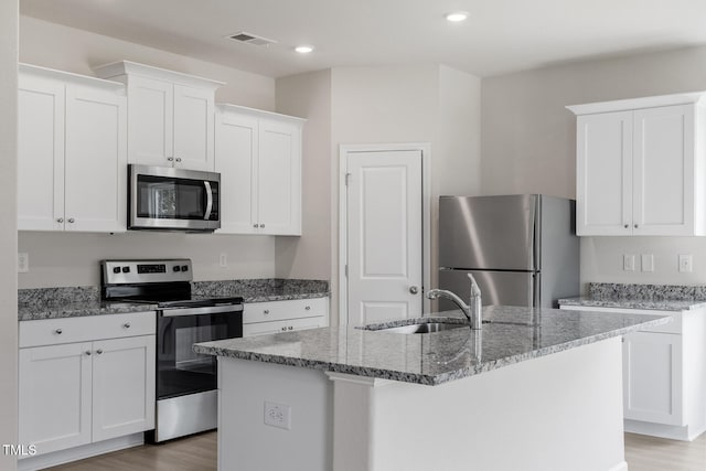 kitchen with a sink, visible vents, appliances with stainless steel finishes, light stone countertops, and a center island with sink