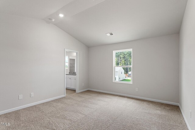 empty room with lofted ceiling, visible vents, baseboards, and light colored carpet