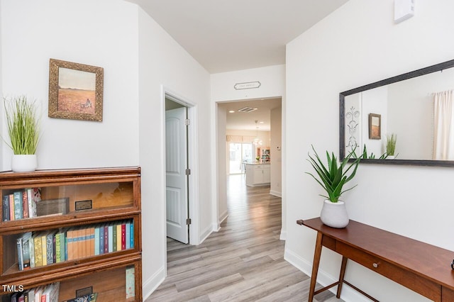 hallway with light wood-style floors, baseboards, and visible vents