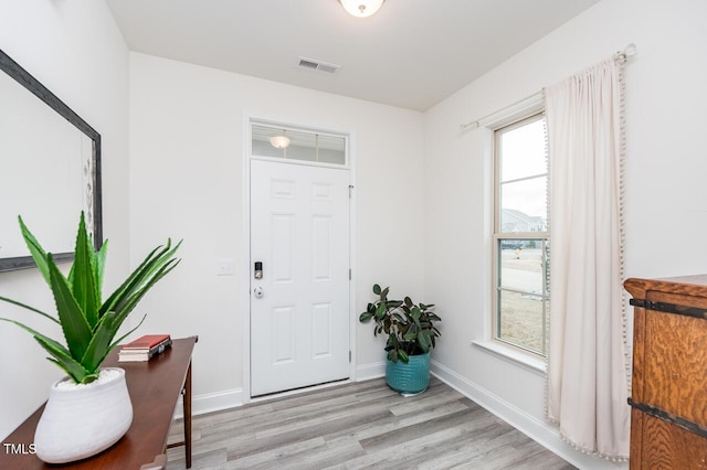 foyer with light wood finished floors, baseboards, and visible vents