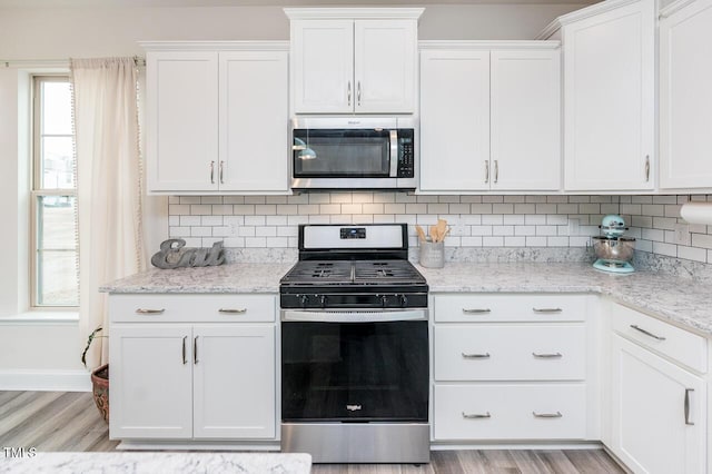 kitchen featuring stainless steel appliances, light wood-type flooring, white cabinetry, and decorative backsplash