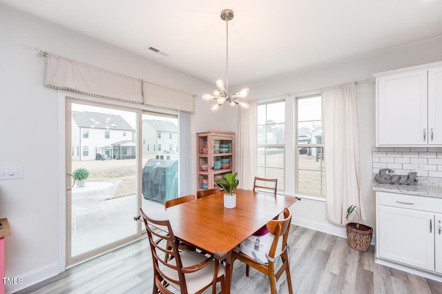 dining room featuring baseboards, light wood-style flooring, visible vents, and a notable chandelier