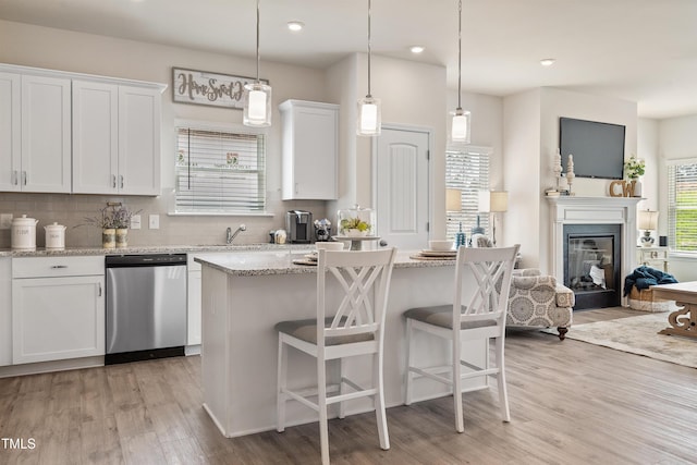 kitchen with light wood finished floors, white cabinetry, backsplash, and stainless steel dishwasher