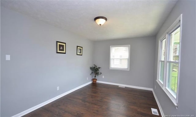 spare room featuring dark wood-style flooring, a healthy amount of sunlight, and baseboards