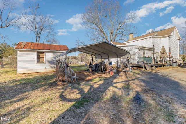 view of yard with an outdoor structure, fence, dirt driveway, a detached carport, and a storage unit