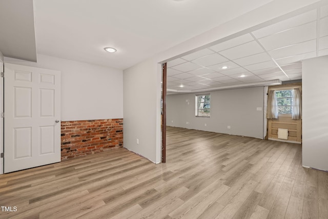 below grade area featuring light wood finished floors, plenty of natural light, and a drop ceiling