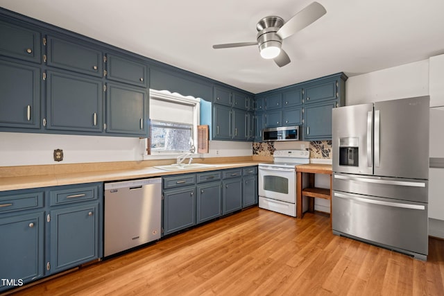 kitchen with a sink, light countertops, blue cabinetry, appliances with stainless steel finishes, and light wood finished floors