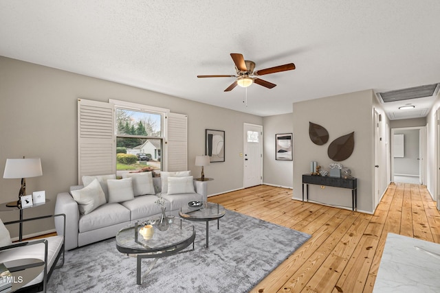 living room featuring visible vents, light wood-style flooring, a textured ceiling, baseboards, and ceiling fan