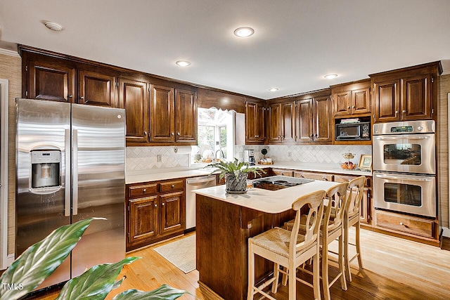 kitchen with a breakfast bar area, tasteful backsplash, light countertops, light wood-style floors, and black appliances