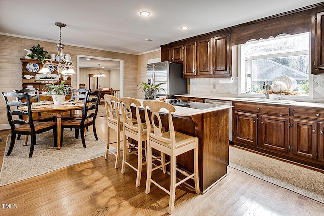 kitchen featuring stainless steel appliances, light countertops, a sink, a chandelier, and light wood-type flooring