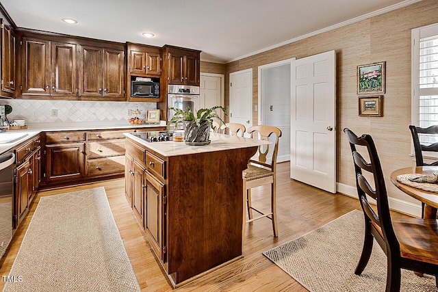 kitchen with light countertops, light wood-style floors, ornamental molding, black appliances, and a kitchen bar