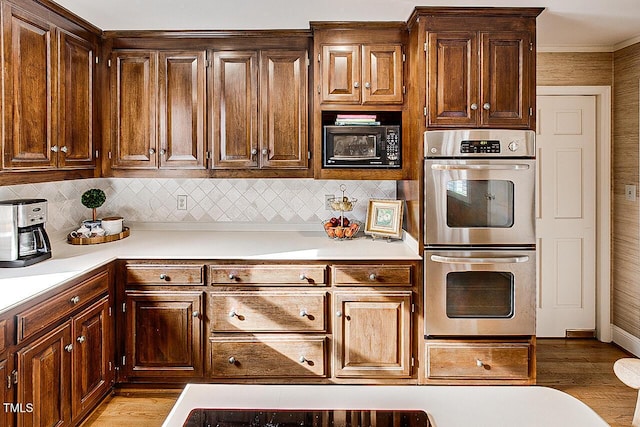 kitchen with light countertops, stainless steel double oven, light wood-type flooring, black microwave, and backsplash