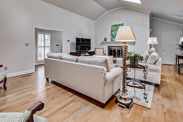 living area with light wood finished floors, visible vents, lofted ceiling with skylight, crown molding, and a brick fireplace