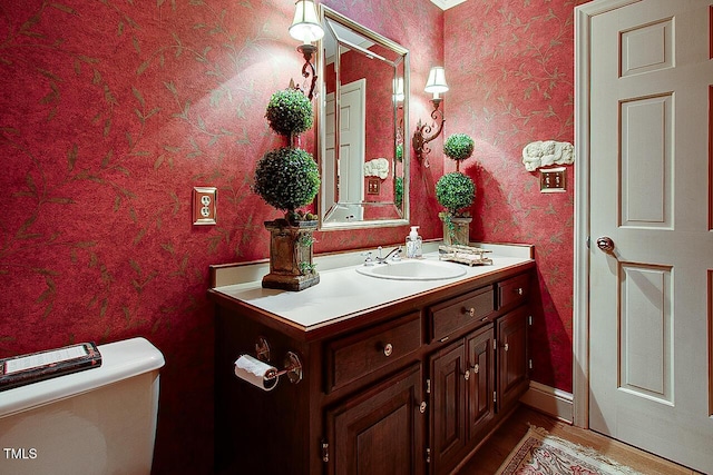 bathroom featuring toilet, wallpapered walls, and vanity