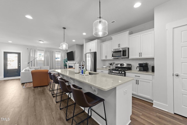 kitchen with dark wood-style flooring, a kitchen island with sink, stainless steel appliances, a kitchen bar, and white cabinetry