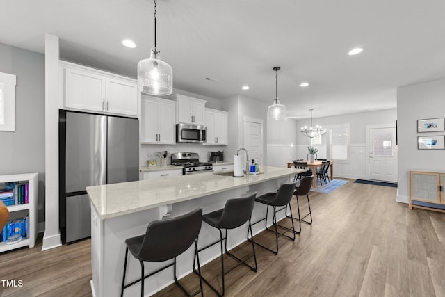 kitchen with appliances with stainless steel finishes, a kitchen island with sink, light wood-type flooring, white cabinetry, and a sink