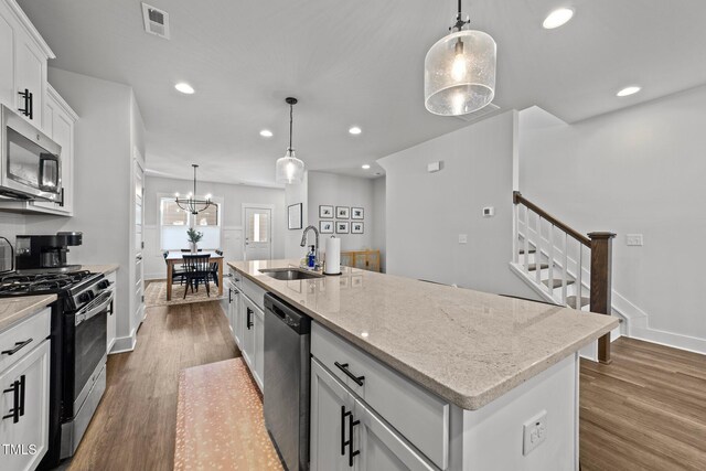 kitchen with dark wood-type flooring, a sink, visible vents, appliances with stainless steel finishes, and a center island with sink