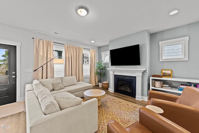 living room featuring visible vents, baseboards, a glass covered fireplace, wood finished floors, and recessed lighting