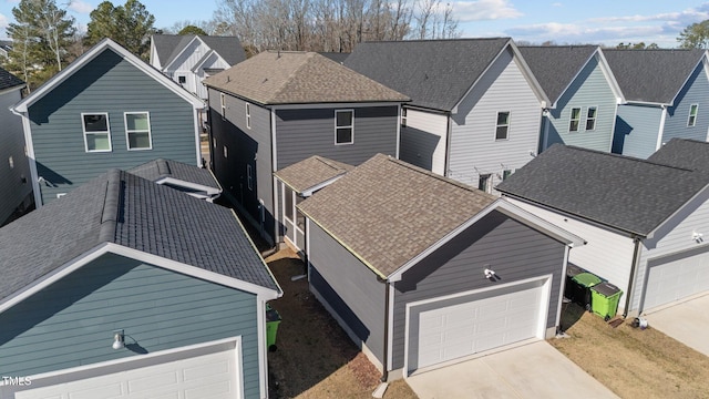 view of front facade featuring a garage, driveway, a shingled roof, and a residential view