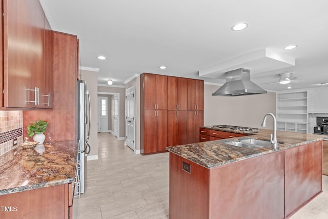 kitchen with a sink, brown cabinets, dark stone countertops, and island range hood