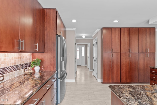 kitchen with dark stone counters, stainless steel fridge, backsplash, and crown molding