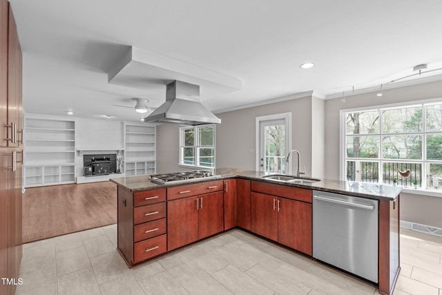 kitchen featuring ceiling fan, dark stone counters, appliances with stainless steel finishes, island exhaust hood, and a sink