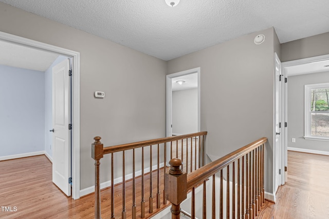 hall featuring an upstairs landing, light wood finished floors, a textured ceiling, and baseboards