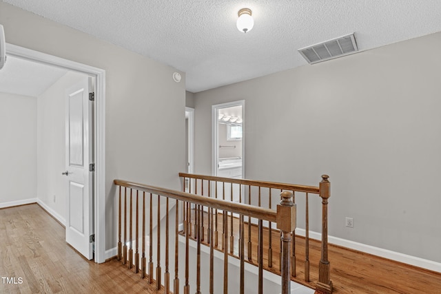 hallway featuring an upstairs landing, visible vents, baseboards, and wood finished floors