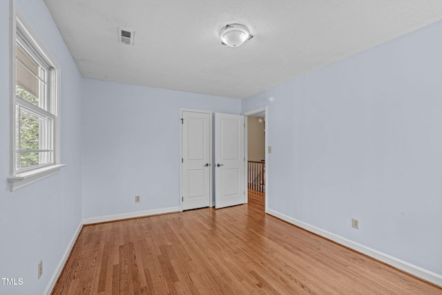 empty room with a textured ceiling, baseboards, visible vents, and light wood-type flooring