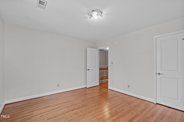 spare room with light wood-type flooring, visible vents, baseboards, and a textured ceiling