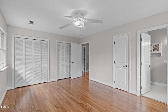 unfurnished bedroom featuring visible vents, baseboards, multiple closets, light wood-style floors, and a ceiling fan