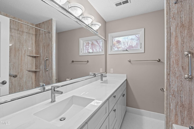 bathroom featuring double vanity, visible vents, a textured ceiling, and a sink