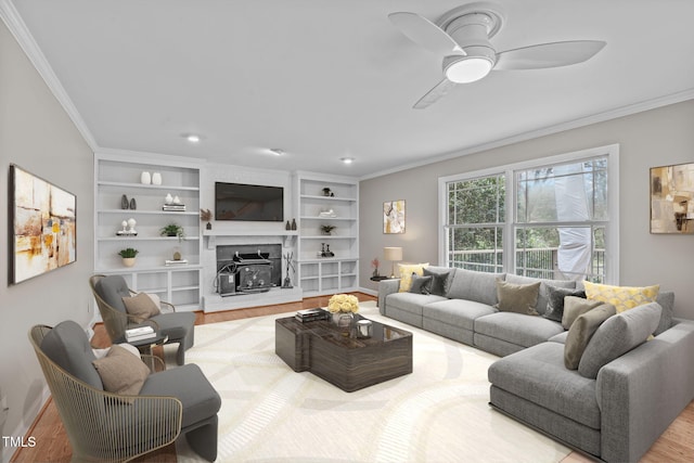 living area featuring ceiling fan, built in shelves, wood finished floors, and crown molding