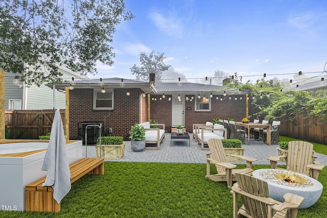 back of property with brick siding, a fenced backyard, an outdoor living space with a fire pit, a yard, and a patio