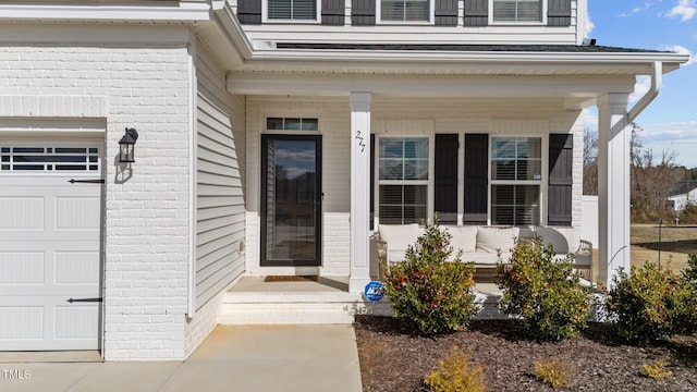 entrance to property with a garage, covered porch, and brick siding