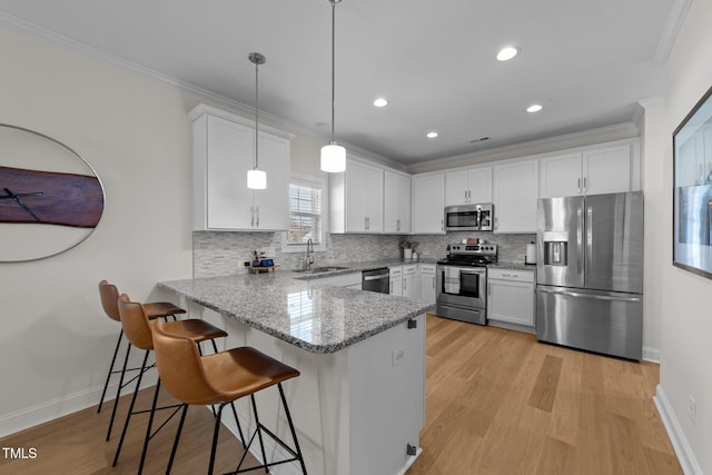 kitchen with ornamental molding, a peninsula, stainless steel appliances, white cabinetry, and a sink