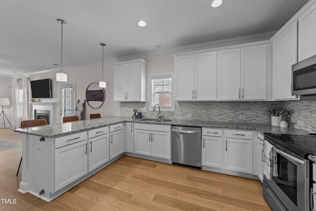 kitchen with stainless steel appliances, a peninsula, a sink, white cabinetry, and light wood finished floors